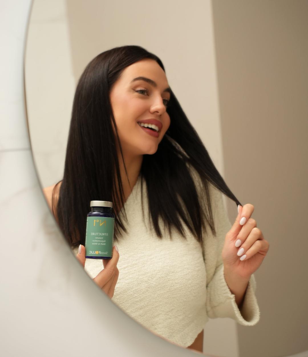 Woman holding capsule bottle, runs her fingers through her hair